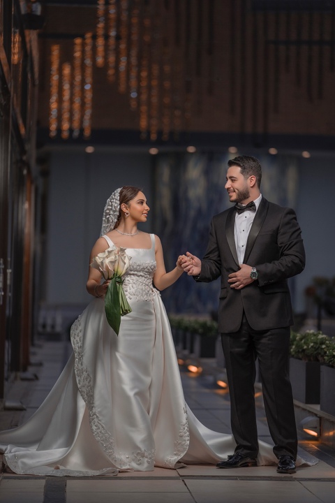 A beautiful couple in wedding attire, the bride in a white dress and the
            groom in a black suit, hold hands.